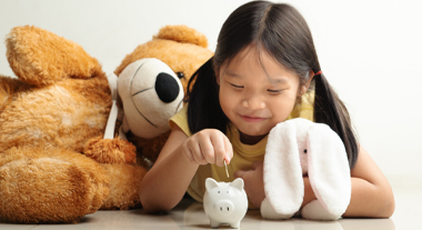 Young girl putting money in piggy bank while sitting with stuffed animals