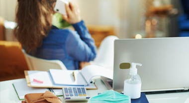 Person on the phone turned away from desk displaying laptop, calculator and papers