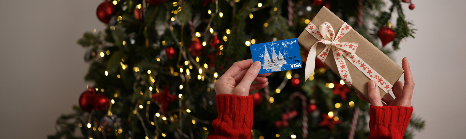 Hands holding up gift card and gift with Christmas tree in the background