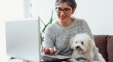 Young person using a laptop which holding her dog