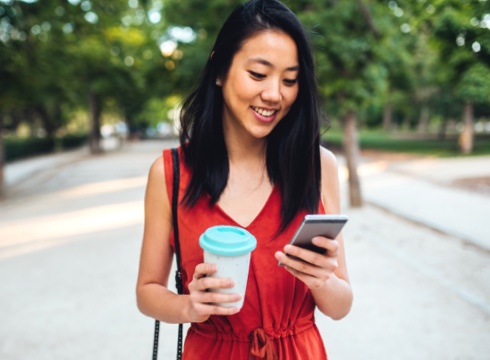 Young person using mobile phone and carrying coffee