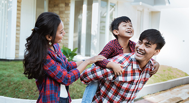 Family playing piggy back in front of house